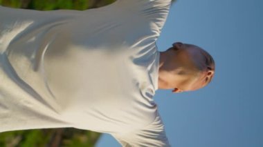 Güneş ışığında yoga yapan güçlü bir adam. Dağ manzarasında nefes alıp veren zinde bir adam. Güzel manzaraya dikey odaklı videoda odaklanmış kel yogi treni. Fitness yaşam tarzı konsepti