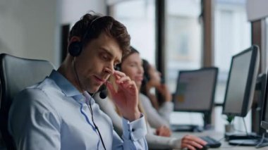 Ciddi bir ajan, müşteri destek ofisinde kulaklık takıyor. Yorgun adam yardım masasında müşteri dinliyor. Düşünceli bir uzman, çözüm talebini sorguluyor. Çevrimiçi yardım hattı kavramı.