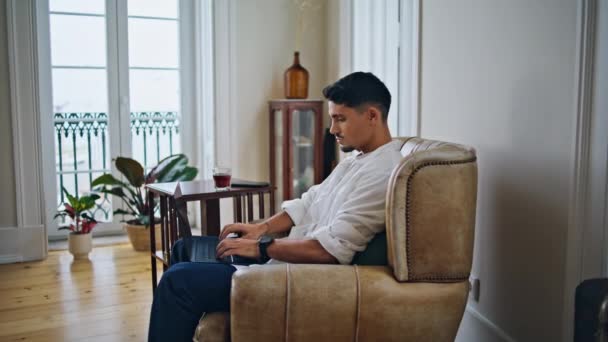居心地の良いアパートでノートパソコンを入力する穏やかな男 リモートでソーシャルメディアを家庭内でチャットするリラックスした男 リビングルームでコンピュータのキーボードをテキストアームチェアに座っているハンサムな男性 — ストック動画
