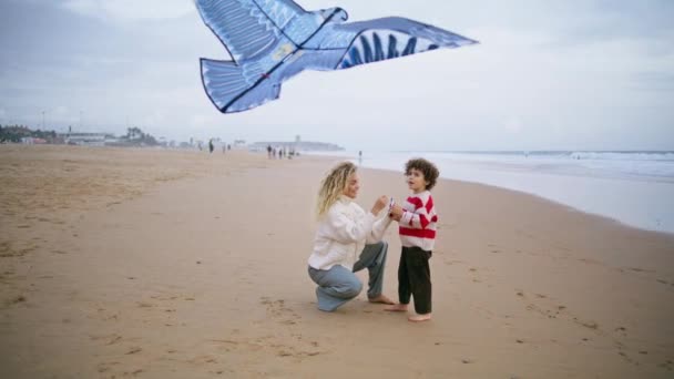 妈妈在风习习的海滨放风筝 有爱心的父母帮助儿子推出玩具 无忧无虑的家人周末在户外享受沙滩上的飞鸟 养育孤独寂寞的母亲和卷曲的孩子 — 图库视频影像