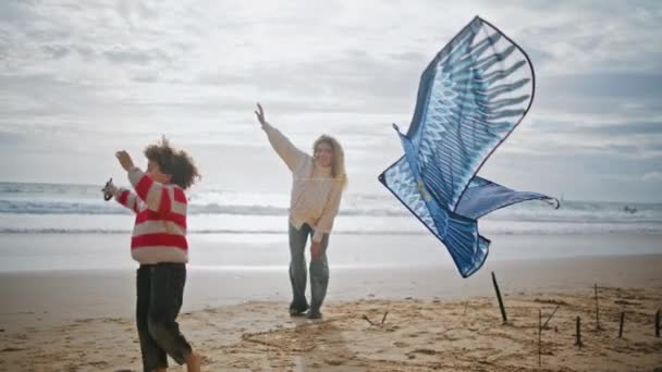妈妈的儿子在多风的海滨放风筝 秋天的周末 一个快乐的女人在帮孩子玩玩具 兴奋的小男孩和保姆一起在海滩上玩耍 支助性的关爱家庭关系 — 图库视频影像