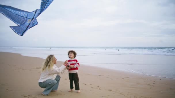 快乐的孩子和妈妈在海滩上放风筝 有爱心的年轻父母帮儿子玩玩具 兴奋可爱的男孩发射飞行鸟休息的周末在风习习海滨 童年抚养记忆 — 图库视频影像