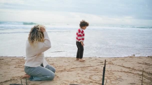 小男孩和妈妈玩海滨游戏 秋天海滩上的家庭周末 卷曲可爱的孩子走在沙滩上 享受海浪中的游戏 单身妈妈临时保姆和孩子们一起度过忧郁的一天 — 图库视频影像
