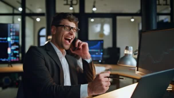 愉快的经理在晚上的工作场所享受打电话的消息 股票快乐人的经纪人在黑暗的办公室里获得了成功的交易利润 成功的商人看上去像电脑庆祝市场的胜利 — 图库视频影像
