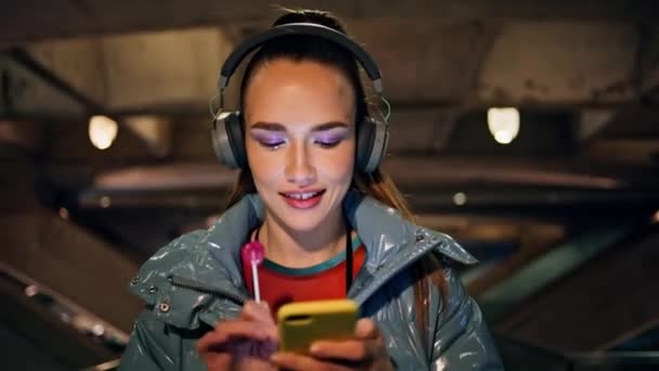 Sonriente Morena Atractiva Escuchando Música Auriculares Inalámbricos Noche Caminar Cerca — Vídeo de stock