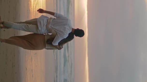 年轻的配偶们在多云的黄昏垂直录像中放松阳光海滩 快乐的恋人手牵手在海滨后视镜前散步 爱女人的男人浪漫的蜜月约会在海边 — 图库视频影像