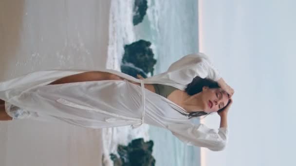 白セクシーなセクシーな垂直ビューで夕方の海岸に立っているケアフリーの女性 海岸で夏の風を楽しむ髪に触れる魅力的なセリーンガール 海の週末にリラックスしたロマンチックな若い女性 — ストック動画