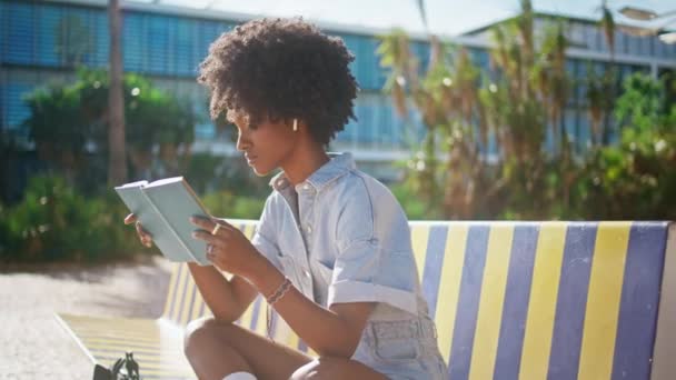 Menina Afro Americana Ler Livro Sentado Banco Rua Colorido Perto — Vídeo de Stock