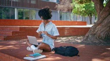 Kulaklık takan Afrikalı kız diz üstü bilgisayarıyla güneşli parkta oturuyor. Kıvırcık ergen öğrenci internetteki dersleri dinlemek için kulaklık takıyor. İnternette okuyan çekici genç bayan..