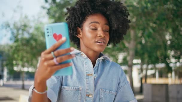 青少年在阳光灿烂的街道上对着智能手机摄像头进行视频通话 快乐的非洲裔美国女孩用手机在网上聊天 微笑的年轻女子在网上记录Vlog内容 — 图库视频影像