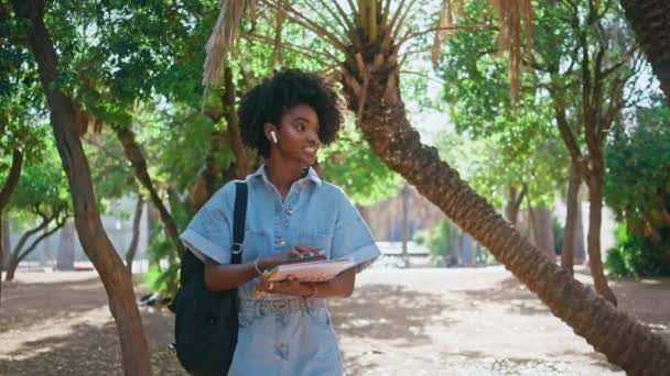 ティーンガールウォーキングキャンパスカレッジは 日当たりの良い日が近づいています 緑の公園で友達と挨拶するかわいいアフリカ系アメリカ人の学生 大学レッスンに行くバックパックと美しい女性ティーンエイジャー — ストック動画