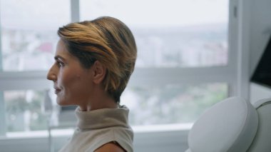 Çekici kadın cilt bakımı için kozmetik kürsüsüne uzanıyor. Modern güzellik kliniğinde cilt muayenesine hazırlanan zarif bayan. Cilt bakımını bekleyen lüks müşteri