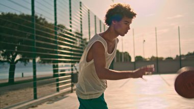 Sportive guy playing basketball on sunlight closeup. Involved teenager jumping training playground alone. Professional sportsman throwing ball at stadium. Urban fitness and healthy lifestyle concept 