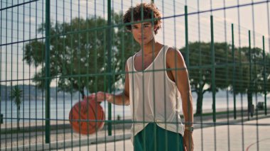 Modern sportsman playing basketball on sports field portrait. Skilful teenager kicks ball at sunny morning stadium zoom on. Serious man looking camera on street closeup. Curly bad guy posing alone 