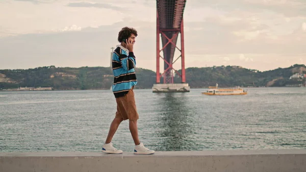 在里斯本堤岸上使用智能手机的游客放松了 4月25日大桥背景的柯莉在讲手机 当代青少年在室外河景中散步 城市生活方式概念 — 图库照片