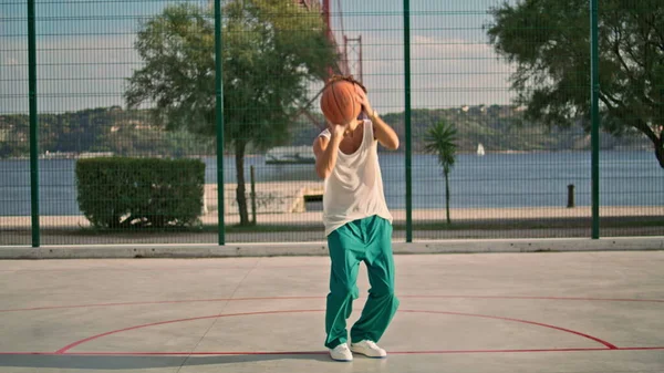 スポーツ場でバスケットボールをしているカーリー男 日当たりの良い朝のスタジアムでバスケットにボールを投げる熟練したティーンエイジャー 都市の遊び場で深刻な学生のアップグレードスキル ストリートを行使する若い男 — ストック写真