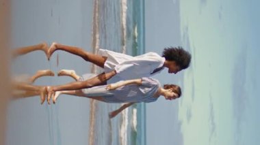 Lgbt çifti okyanus kıyısında dikey çekim yapıyor. Kaygısız arkadaşlar yaz tatilinde kumsalda yürümekten hoşlanırlar. Gülümseyen çok ırklı kadınlar deniz kıyısında haberleri paylaşıyorlar. Kızlar arası eğlence