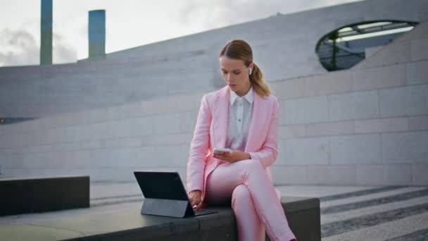 ストリートベンチに座っているタブレットでリモートで働く女性の専門家 屋外でラップトップ画面を見ているエレガントな自信あるビジネスマン コンピュータでスマートフォンタイピングを保持するヘッドフォンに焦点を当てた女性 Ceo — ストック動画
