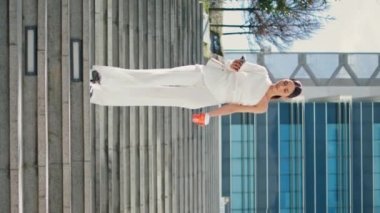 Zarif kadın aşağıda akıllı telefon ekranına bakıyor. Güneşli bir gün dikey videosu. Genç iş kadını telefonda kahve fincanı ile merdivenlerden inerken mesajlaşıyor. Telefon kullanan lüks bir kadın.