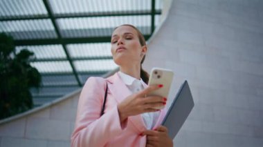 İş kadını telefon haritasını kullanarak çevreyi kolaçan ediyor. Açık havada cep telefonu uygulamasına bakan zarif, kendine güvenen bir kadın. Elinde belge klasörü tutan çekici bayan akıllı telefonu kaydırıyor..