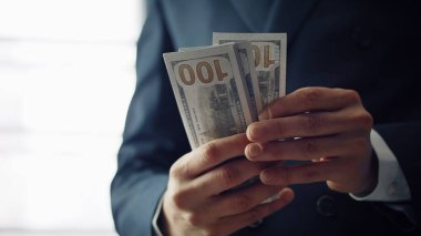 Closeup hands counting cash american dollars indoors. Unrecognizable successful man in luxury black suit calculating financial profit high income business payment. Young businessman having pack money.