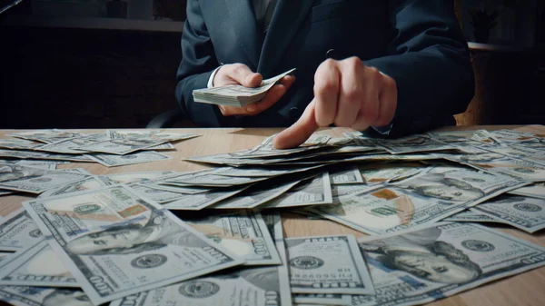 未知の豊かな男のヒープ私たちのエレガントなスーツを閉じるにはオフィスの机に座ってドルを数える ビジネスマンの手には百枚の紙幣が山の上に置かれている マネージャー — ストック写真