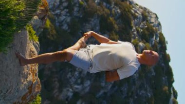Yogacı adam okyanus uçurumunda egzersiz yapıyor. Odaklanmış sporcu doğanın dikey videosunda güneş ışığında meditasyon yapıyor. Güçlü adam Asana 'yı oynuyor.. 