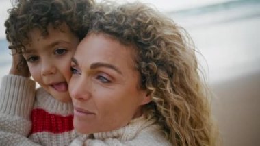 Mutlu anne, sonbahar kumsalında oğlunu öpüyor. Şirin kıvırcık çocuk ailesiyle eğleniyor. Güzel kadın anne okyanus kıyısında neşeli çocuğa sarılıyor. Aile ilişkileri kavramını sevmek