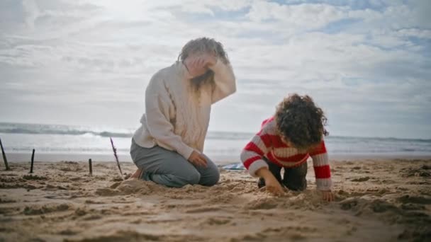 年轻妈妈和可爱的男孩在海滩玩耍 快乐的家庭一起建造沙堡 漂亮的家长保姆和学龄前儿童一起享受秋天的周末 度假游戏的概念 — 图库视频影像
