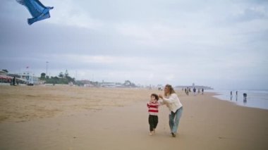Mutlu anne, güzel oğluyla birlikte sonbahar kumsalında uçurtma oyuncağı fırlatıyor. Kaygısız ebeveyn, sahil şeridinde küçük çocukla oynamaya yardım ediyor. Neşeli bir aile haftasonu tatilini deniz kıyısında geçiriyor..
