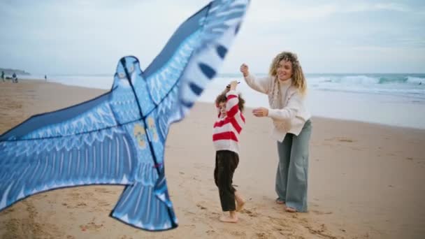 一家人一起在风习习的海滨放风筝 快乐的母亲与儿子在海滩共度周末 漂亮的临时保姆帮助教兴奋的孩子玩玩具 快乐的母性概念 — 图库视频影像
