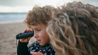 Yakından bir çocuk okyanus kıyısında dürbün görüyor. Gülen aile, sonbahar tatilini sahilde geçirip dışarıda dinleniyor. Mutlu bekar anne, sevimli kıvırcık oğluyla oynarken eğleniyor. Ebeveyn bağlanma anları