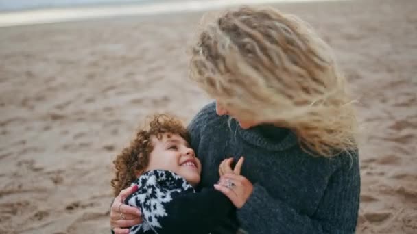 可爱的妈妈和可爱的小儿子在海滩特写镜头里玩得很开心 与年轻漂亮的父母保姆共度愉快的周末 在海滨举行的秋季野餐上 一家人欢欢喜喜地拥抱在一起 — 图库视频影像