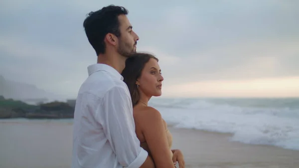 性感的情人喜欢海风雨雨的海滩特写 性感女人面对镜头的肖像 两个新婚夫妇拥抱在岸边 在浪漫的约会中 多民族的情人拥抱在一起 爱情伴侣注视着大海 — 图库照片
