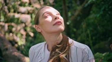 Kapalı, sakin kadın yaz güneşinin altında orman yeşilliklerinde parlıyor. Doğa güzelliğine bakan mutlu nazik bir kızın portresi güzel bir parkta oturuyor. Sakin romantik bayan bahçede dinleniyor..