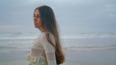 Sensual woman looking camera at ocean coast closeup. Calm lady watching misty evening nature alone. Female person enjoying stormy sea view. Serious tourist delighting marine landscape at single travel