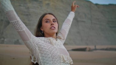 Romantic lady relaxing evening seashore. Sexy woman raising hands to sky stretching body at summer vacation. Female person meditating at sandy beach. Tranquility and connect with nature concept 