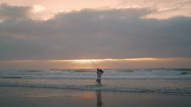 Beautiful pair spinning morning sea beach. Happy people rejoicing together at cloudy nature. Romantic lovers embracing each other at ocean waves. Cheerful couple celebrate honeymoon sunrise horizon