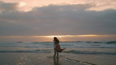 Married lovers having fun at sunbeams coastline. Cheerful man woman spinning at sandy beach. Young couple rejoicing in misty ocean. Lovely newlyweds enjoying time together on honeymoon anniversary