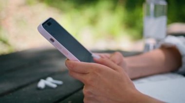 Kadın elleri cep telefonu daktilo ediyor. Güneşli doğada mesaj yolluyor. Kapatın. Tanımlanamayan bir kız modern akıllı telefon kullanarak mesaj atıyor. Park ahşap masasında oturuyor. Dışarıdaki cep telefonuna mesaj atan bir kadın..