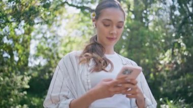 Ormanda müzik dinleyen akıllı telefon uygulaması kullanan romantik bir kadın. Kablosuz kulaklıklı çekici kız cep telefonuyla güneşli parkta geziniyor. Cep telefonu tutan mutlu sakin bayan..