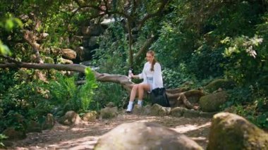 Ağaç gövdesinde oturan romantik kız yeşil, kalın ormanda yatıyor. Genç aktif kadın hafta sonundan sonra güzel doğa yürüyüşünden sonra dinleniyor. Kaygısız mutlu bayan gezgin yaz tatilinde park güzelliğinin tadını çıkarıyor..