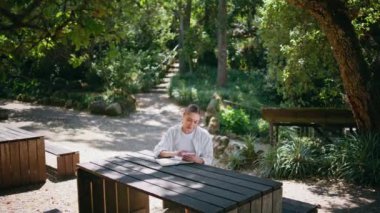 Park masasında oturan akıllı telefonlu bir kadın internetten not defterine bilgi yazıyor. Doğada mobil eğitim uygulaması kullanan düşünceli güzel bir bayan. Ormandaki kitapçıda notlar alan tatlı kız..