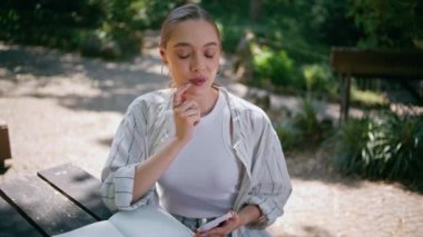 Güzel bir kadın akıllı telefonuyla park masasında oturan not defterine mesaj yazıyor. Mobil interneti doğa üzerinde kullanmayı düşünen yaratıcı bir iş kadını. İnternette okuyan güzel bayan..