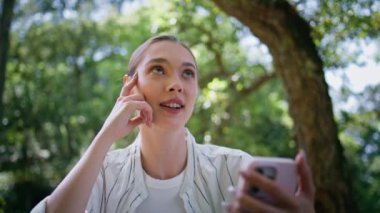 Akıllı telefondan konuşan bir kadın yeşil park ağaçlarının altında oturuyor. Çekici kaygısız kız güneşli bir günde cep telefonuyla konuşuyor. Şirin bayan serbest çalışan cep telefonunda sohbet ediyor.