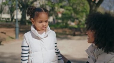 Mutlu anne aile hafta sonunda kızla iletişim kuruyor. Yakın plan. Gülümseyen Afrikalı Amerikalı kadın güneşli parkta küçük çocukla konuşuyor. Güzel anne, sonbahar doğasında sevimli kızıyla rahatlıyor..