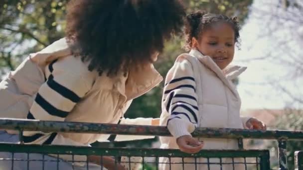 アフリカ系アメリカ人の母親が日当たりの良い公園で笑っている 明るくリラックスした家族で 同じ白いジャケットを着てリラックス 笑顔の若い女性が少女をくすぐった 幸福のコンセプト — ストック動画