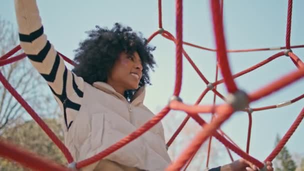 近代的な遊び場でロープピラミッドで娘と遊ぶ遊び心のある母親 アフリカ系アメリカ人の家族が週末にアウトドアで活躍する笑顔 共同スポーツ活動コンセプト — ストック動画