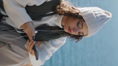 Okyanus yamacında dikey müzik dinleyen güzel kız. Sakin kadın sakin deniz manzarasında favori şarkının keyfini çıkarıyor. Stressiz gezgin bahar tatilinde dinleniyor. Hobi huzurlu ruh hali