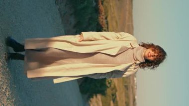 Sonbahar güneşi altında dikey yürüyen rahat bir kız. Gülümseyen kadın akşam çayırına giden doğa manzarasından zevk alıyor. Serene turist dışarıda dinleniyor. Rahatlatıcı hafta sonu konsepti.